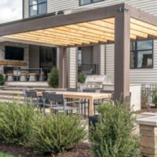 Trendy outdoor patio pergola shade structure, awning and patio roof, dining table, chairs, metal grill surrounded by landscaping